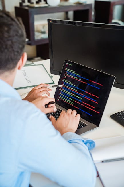 A close-up photograph shows a laptop computer open on a wooden desk, displaying lines of programming code in a dark-themed editor. To the right of the laptop, there is a ceramic coffee mug with a beig